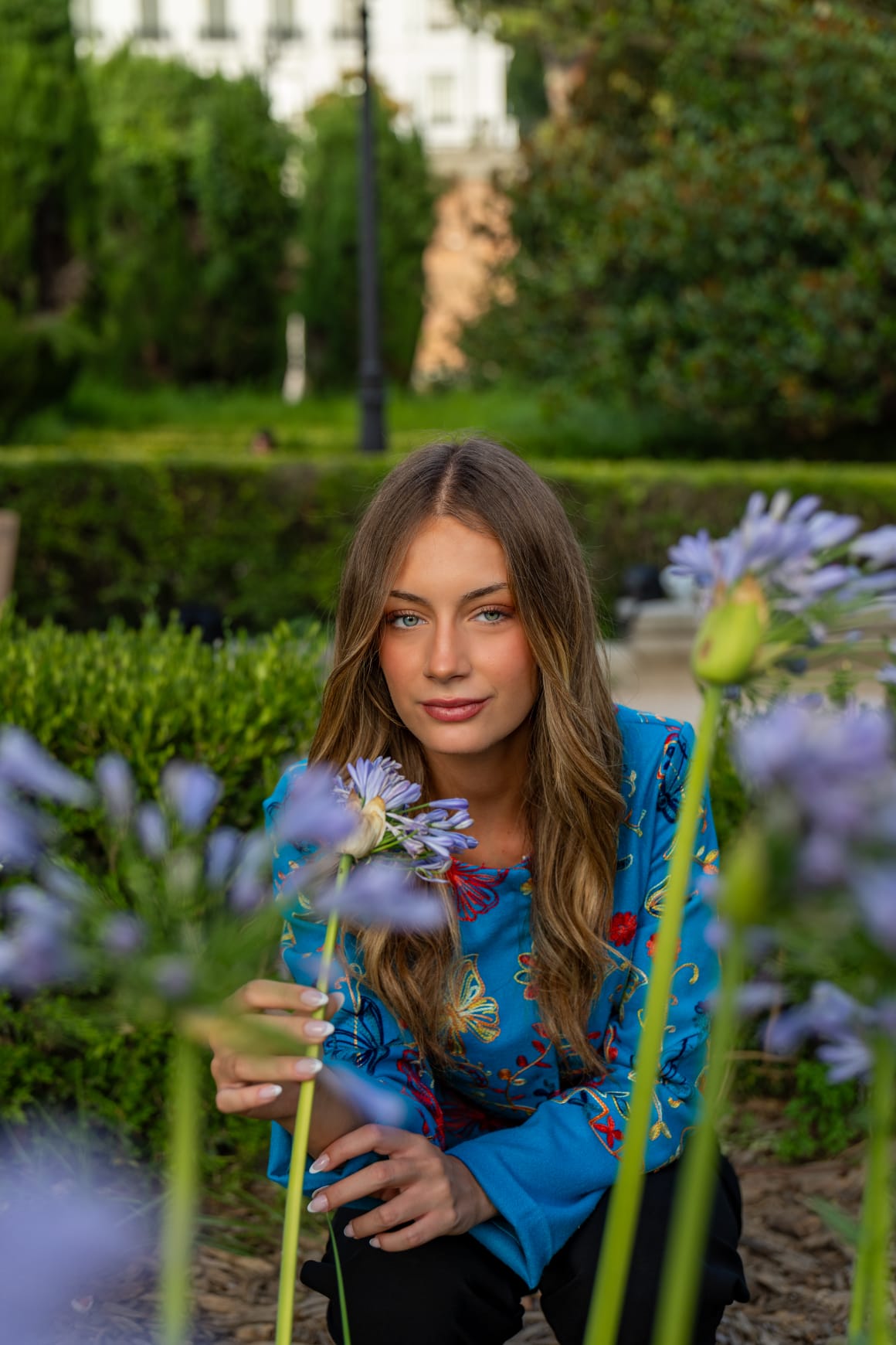 Torera turquesa bordada con mariposas y flores, retrato entre agapantos en jardines del Palacio Real de Madrid