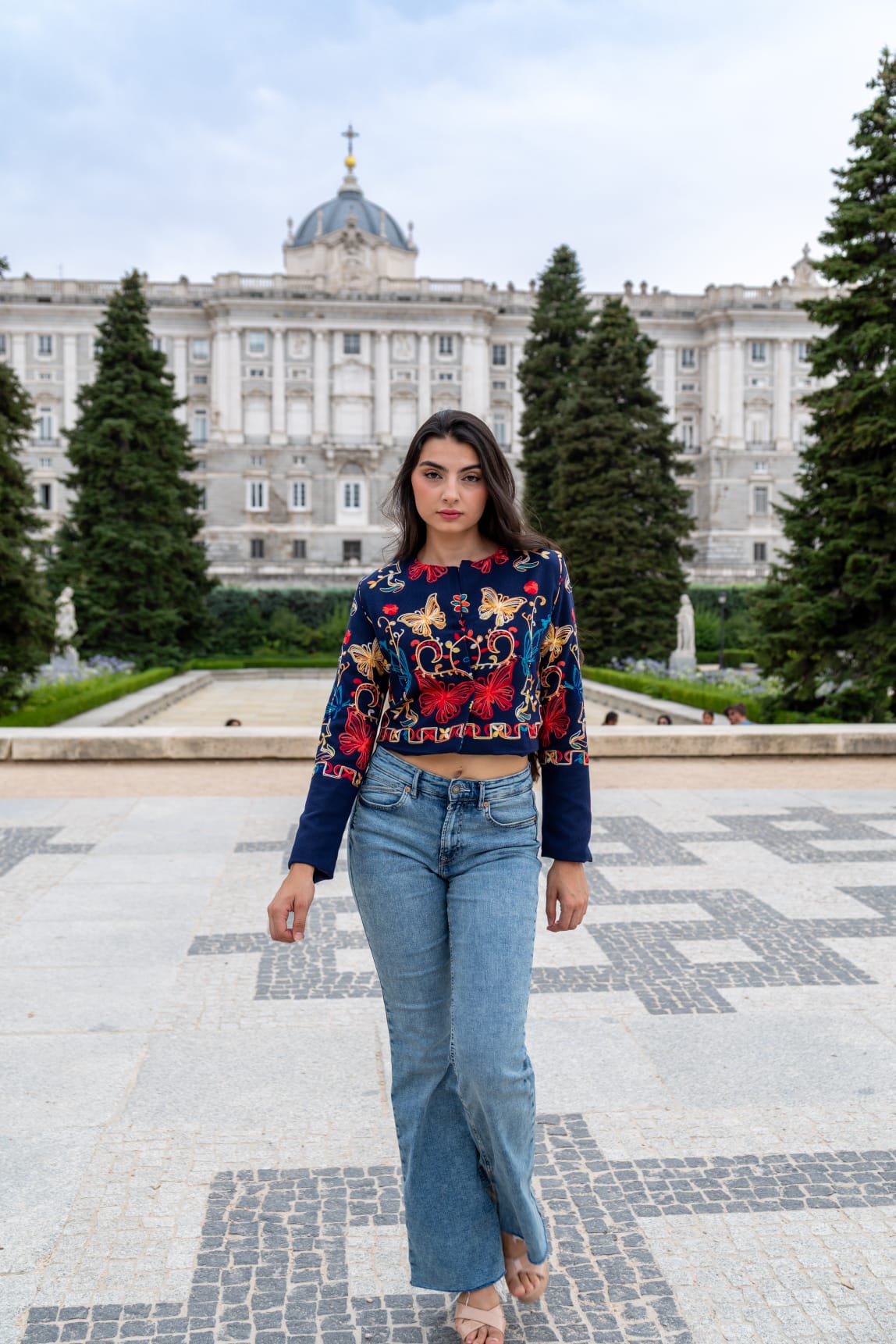 Torera azul marino bordada con mariposas multicolor, modelo con vaqueros frente al Palacio Real de Madrid