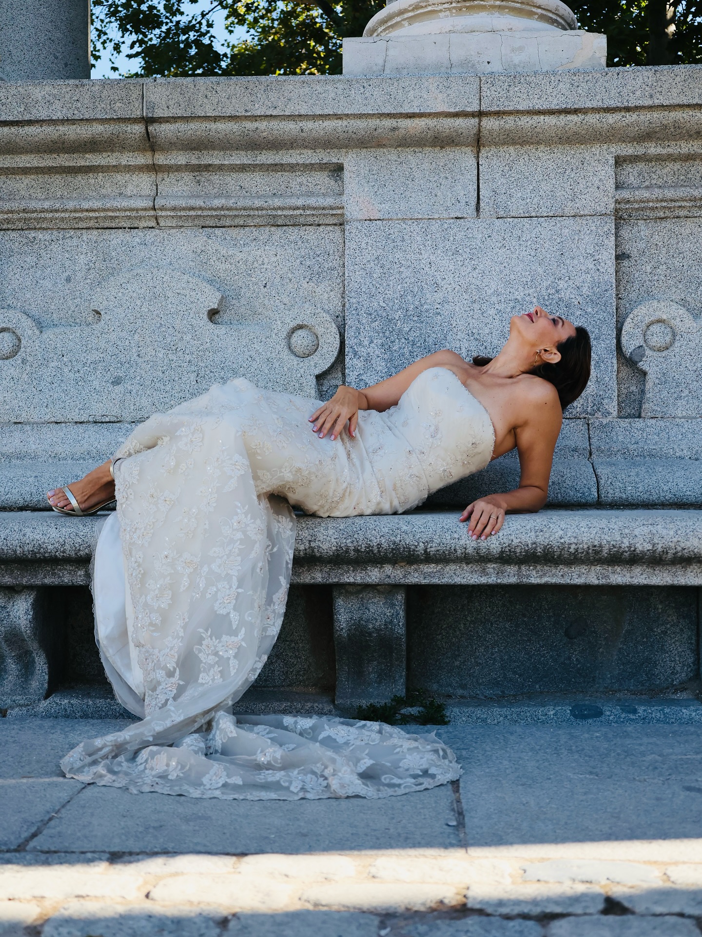 Vestido de novia a medida de encaje bordado, tomada de perfil sobre banco de piedra