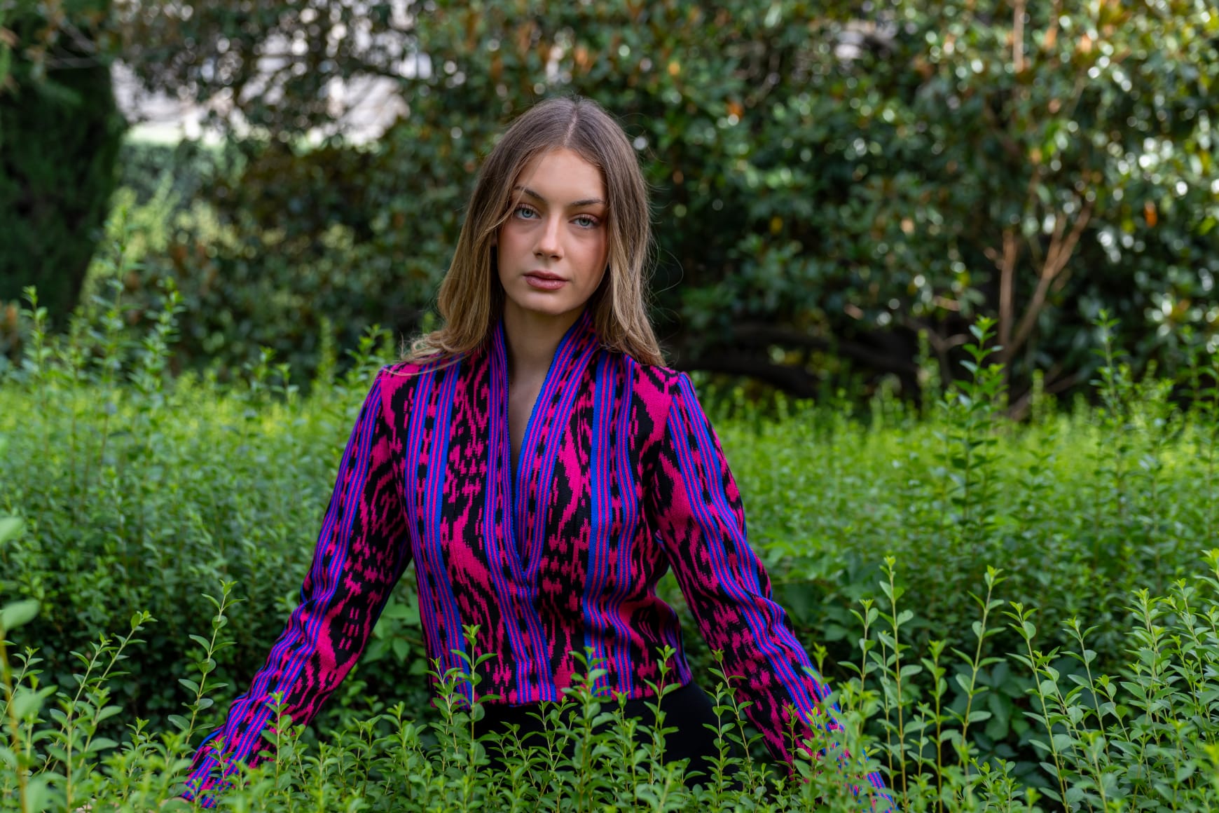 Torera ikat fucsia, azul eléctrico y negro con cuello alzado, modelo entre vegetación en jardín