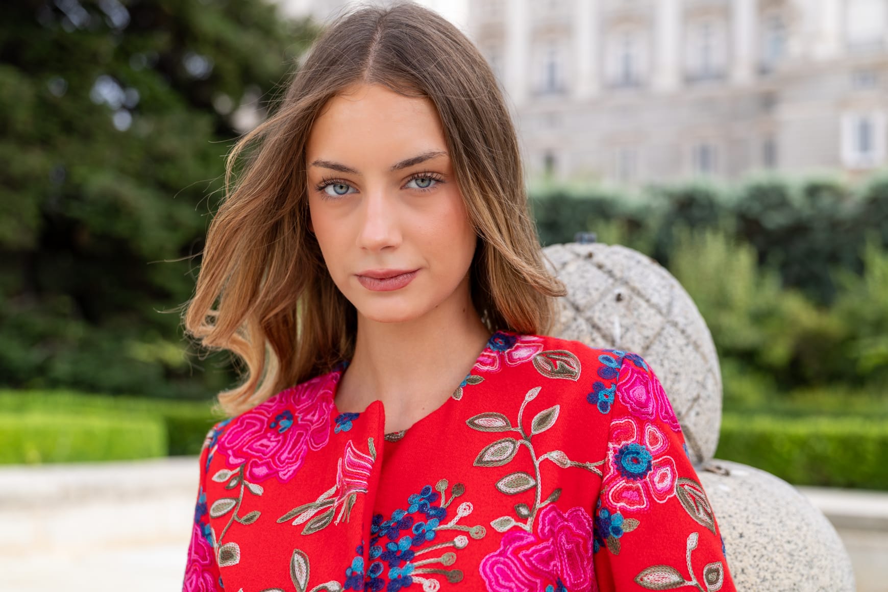 Torera roja bordada con flores fucsia y azules, retrato de primer plano en jardines del Palacio Real de Madrid