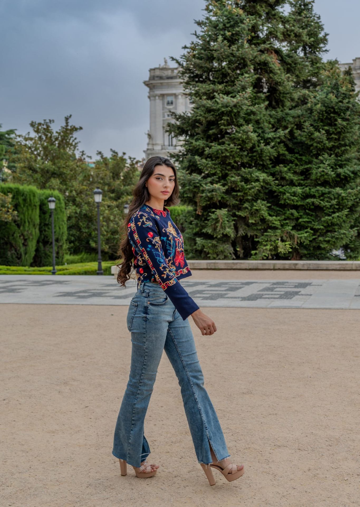 Torera azul marino bordada con mariposas multicolor combinada con vaqueros acampanados, modelo caminando en jardines de Madrid